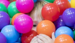 Photo: A child's face can be seen between many colourful balls in a ball pool