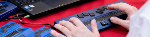 Photo: Hands typing on a Braille display connected to a laptop